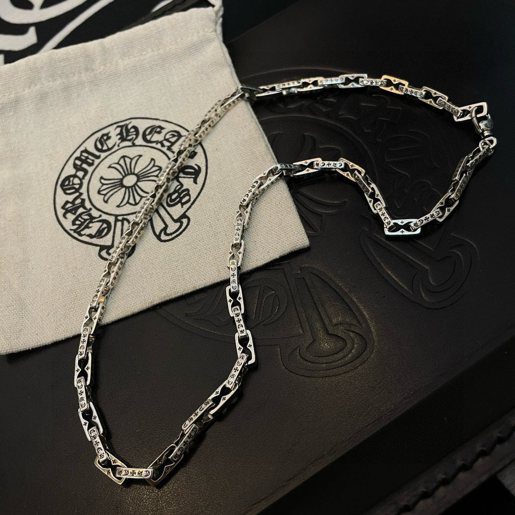 Silver chain necklace on black and cream pouches with embossed symbols