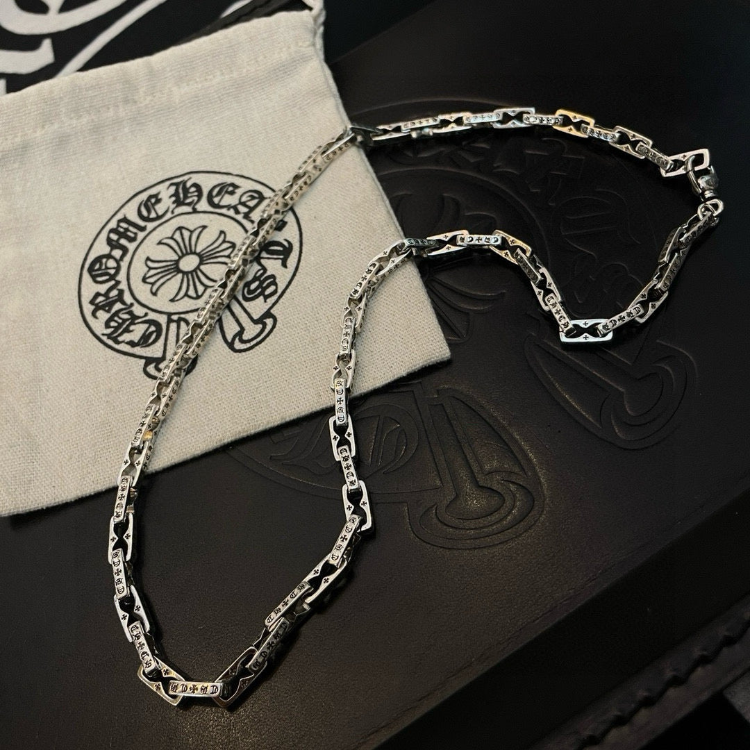 Silver chain necklace on black and cream pouches with embossed symbols