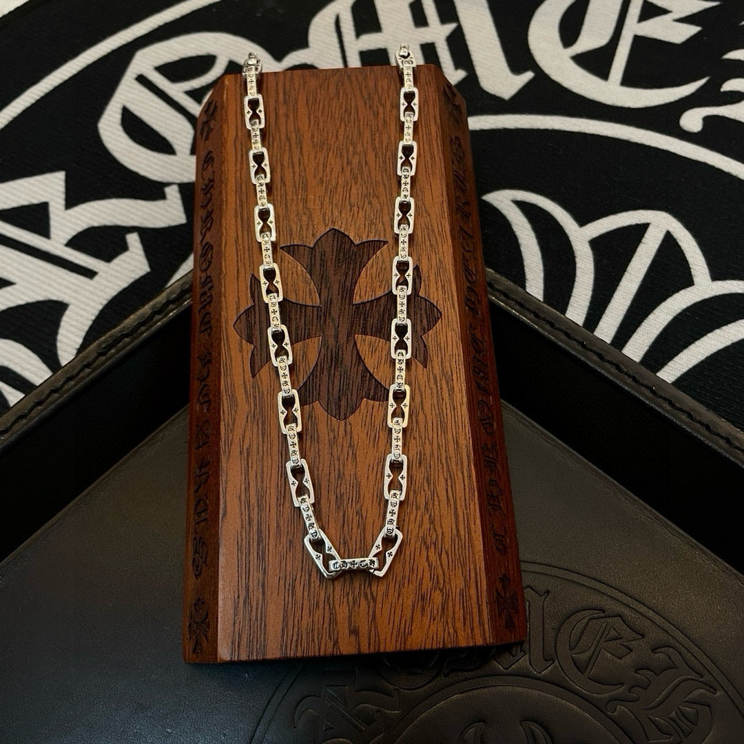 Silver chain necklace on wooden box with butterfly-style emblem