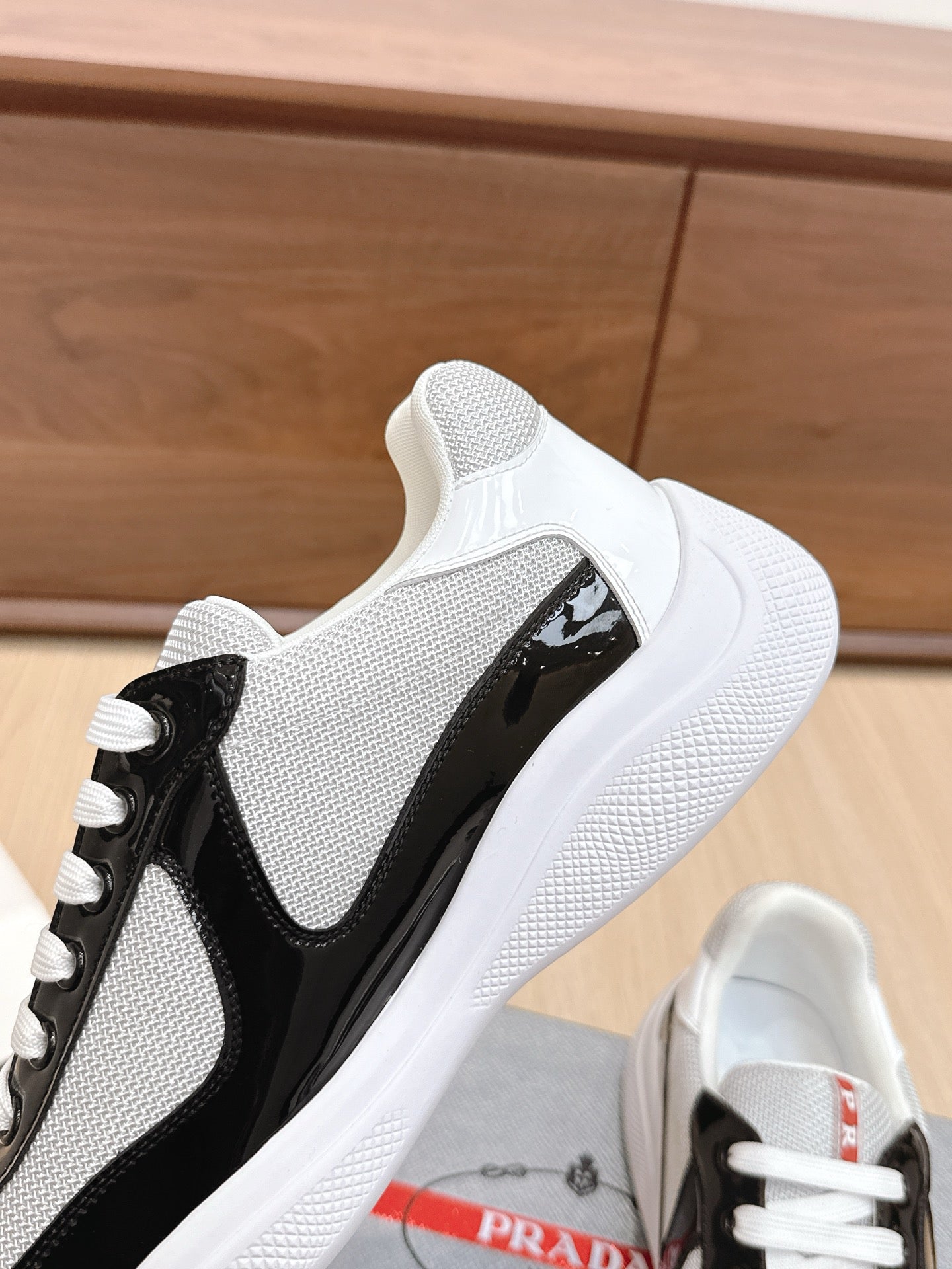 Prada unisex sneaker side view: white mesh with black insert, white laces.