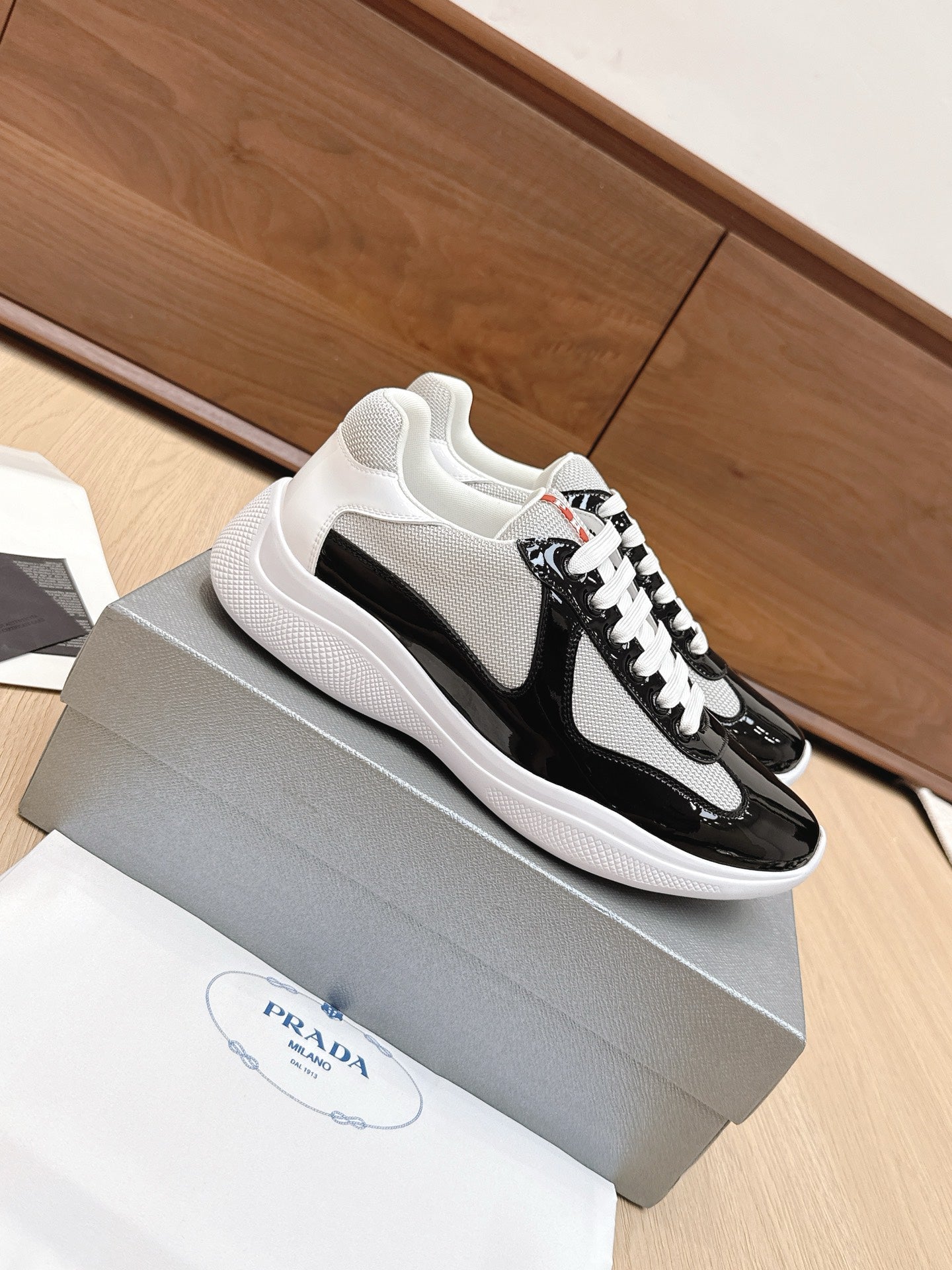 Prada unisex sneakers on box: white mesh side, black upper, white laces.