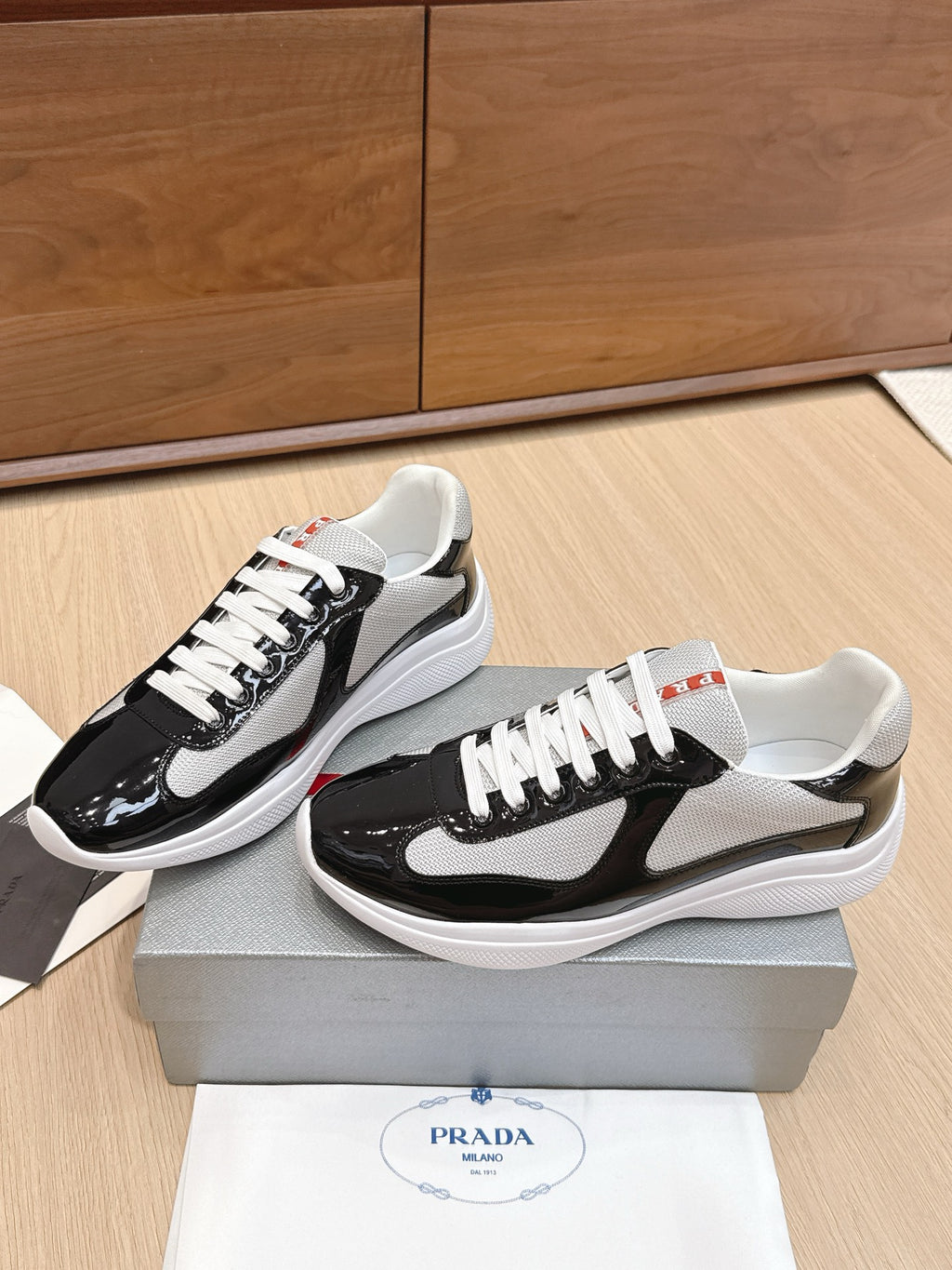 Prada unisex sneakers, angled view: black patent leather with white laces and gray mesh
