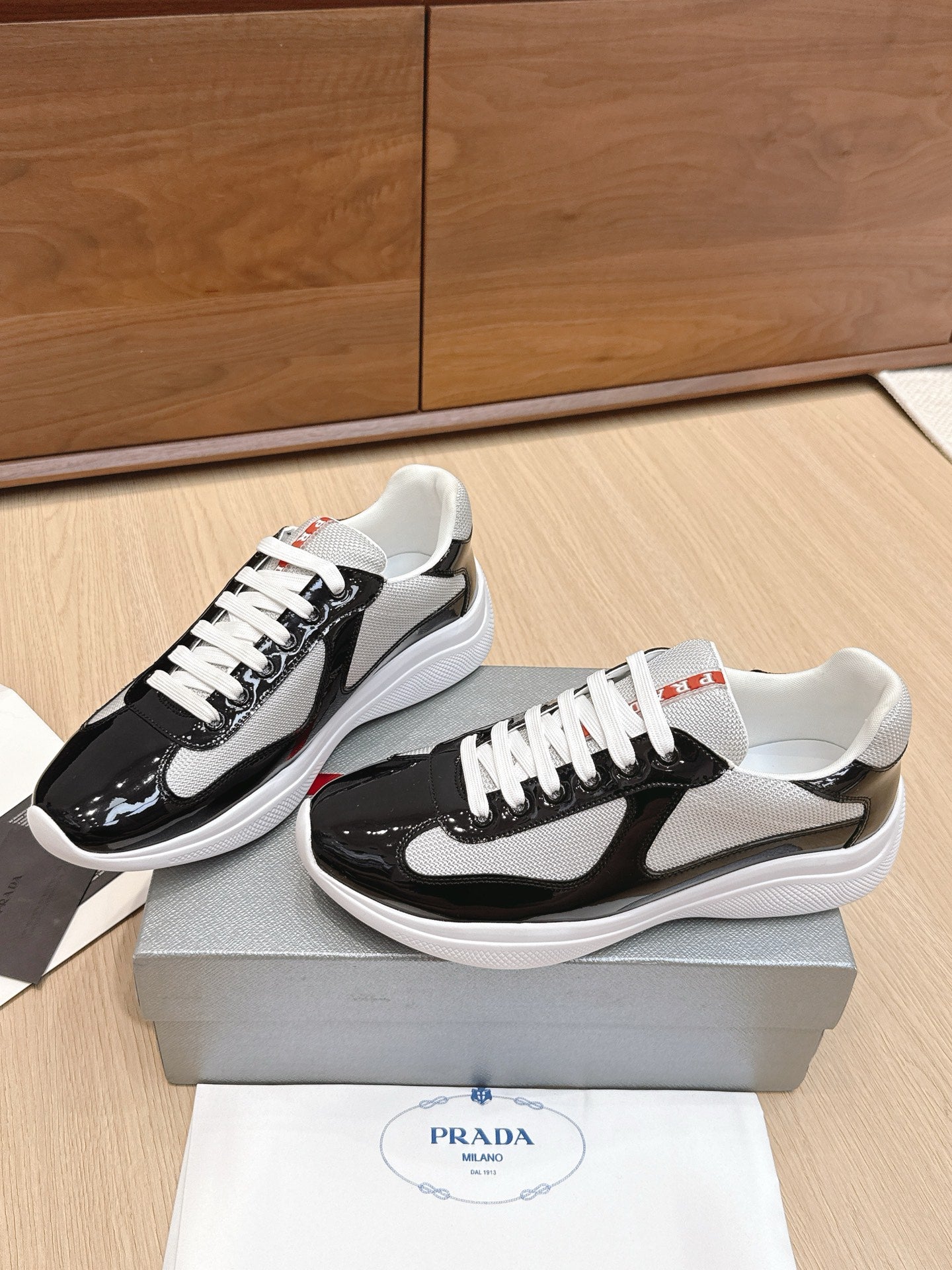 Prada unisex sneakers, angled view: black patent leather with white laces and gray mesh