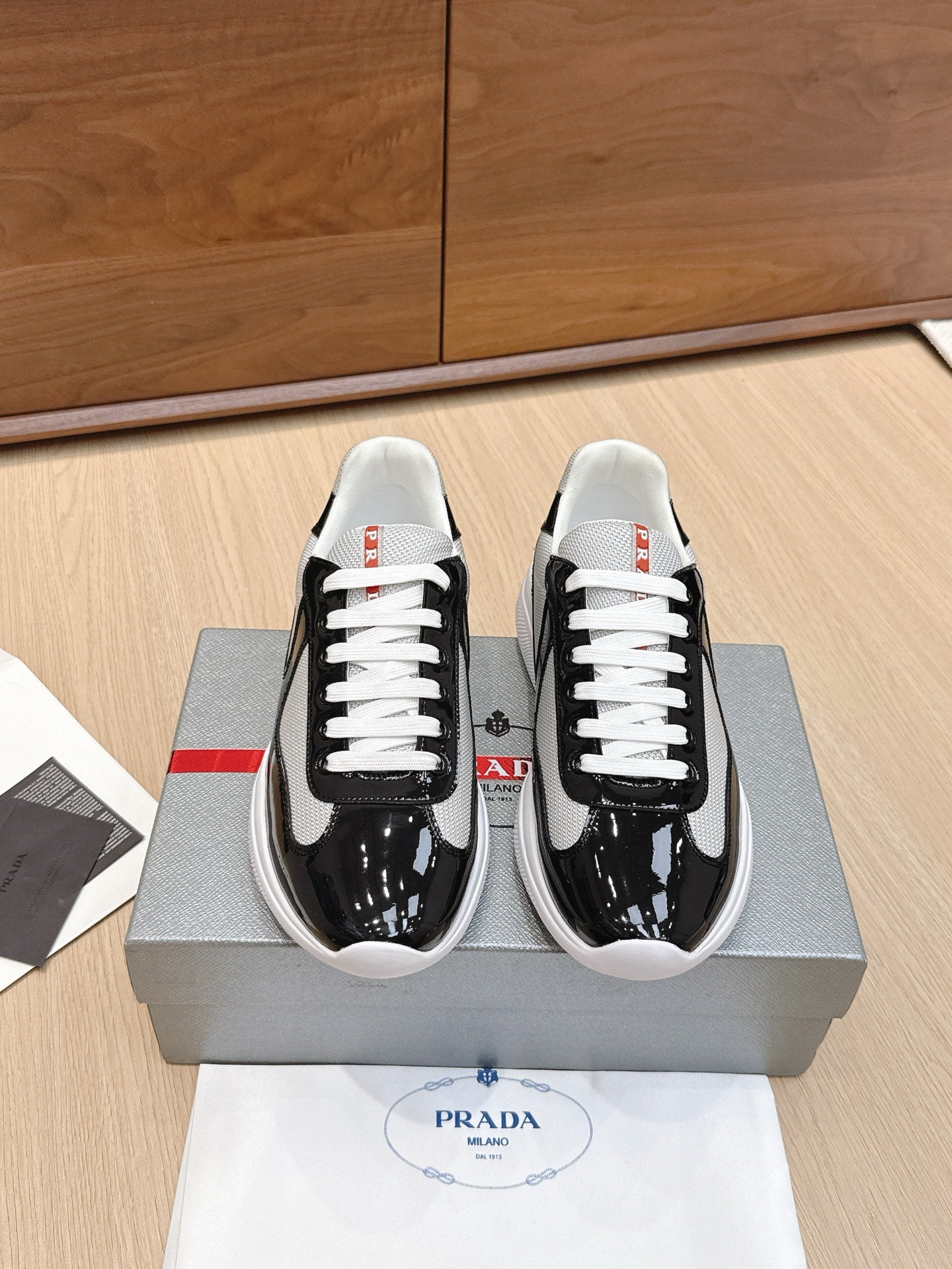 Prada unisex sneakers in black patent leather with white laces and red tag detail
