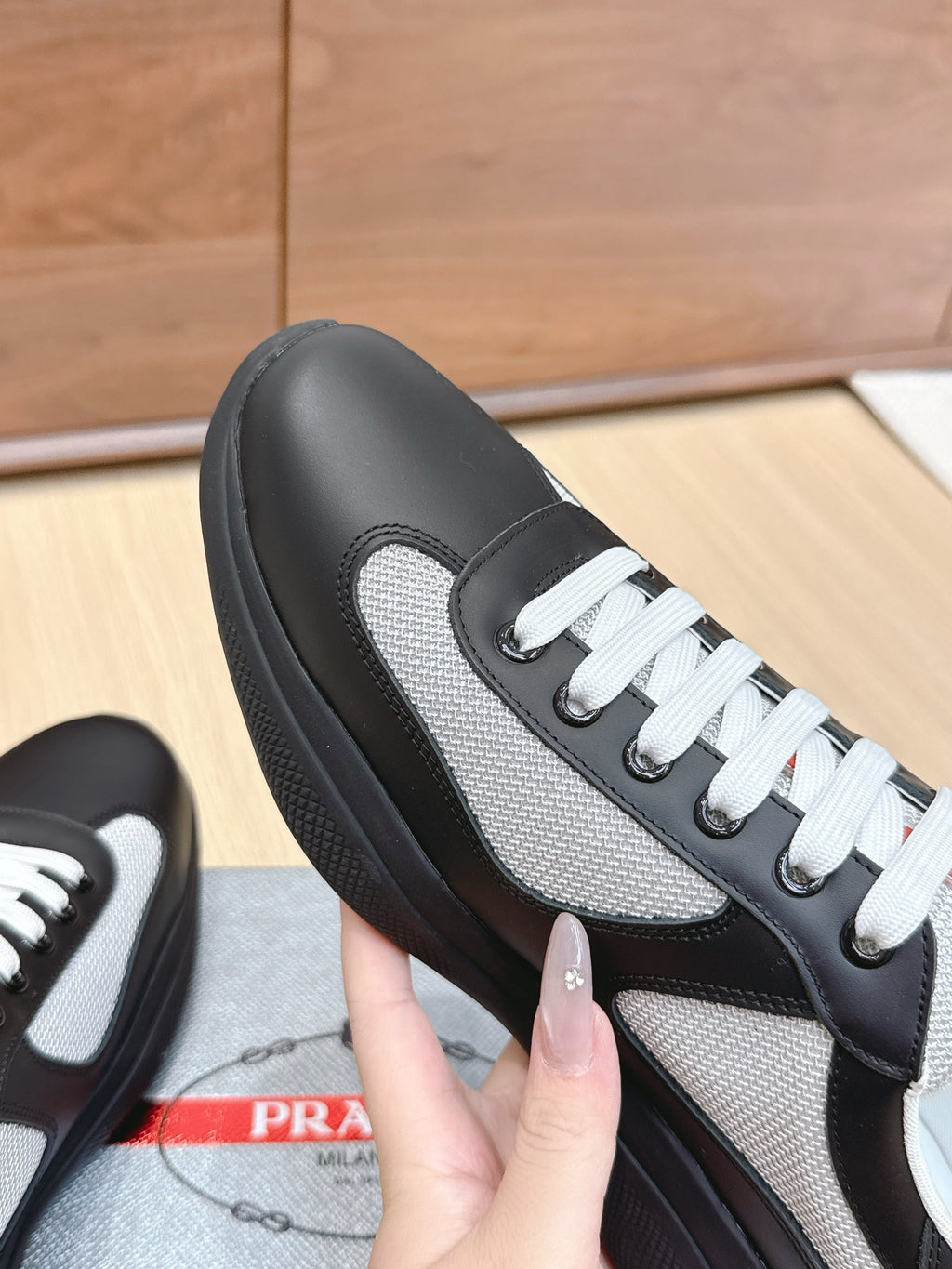 Prada unisex sneaker close-up: black leather and grey mesh side with white laces