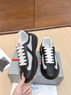 Prada unisex sneakers, black with white laces and white trim; hand holding pair