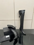 Knee-high black boots with pointed toe and stiletto heel, lace-tie tassel accents