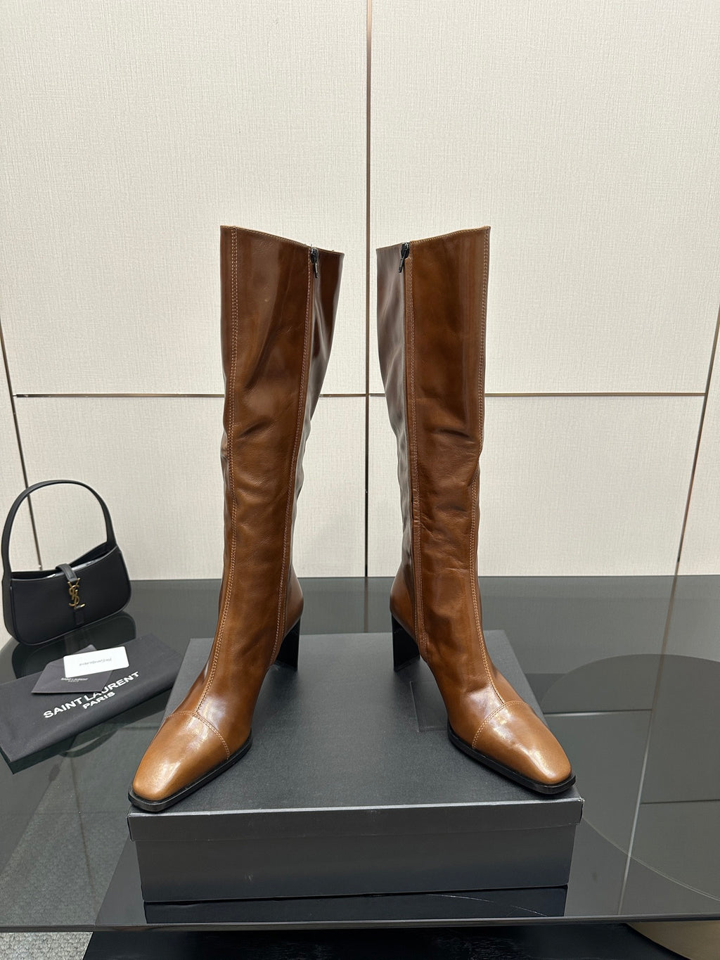 Brown knee-high leather boots with pointed toe and slim heel, paired on display box