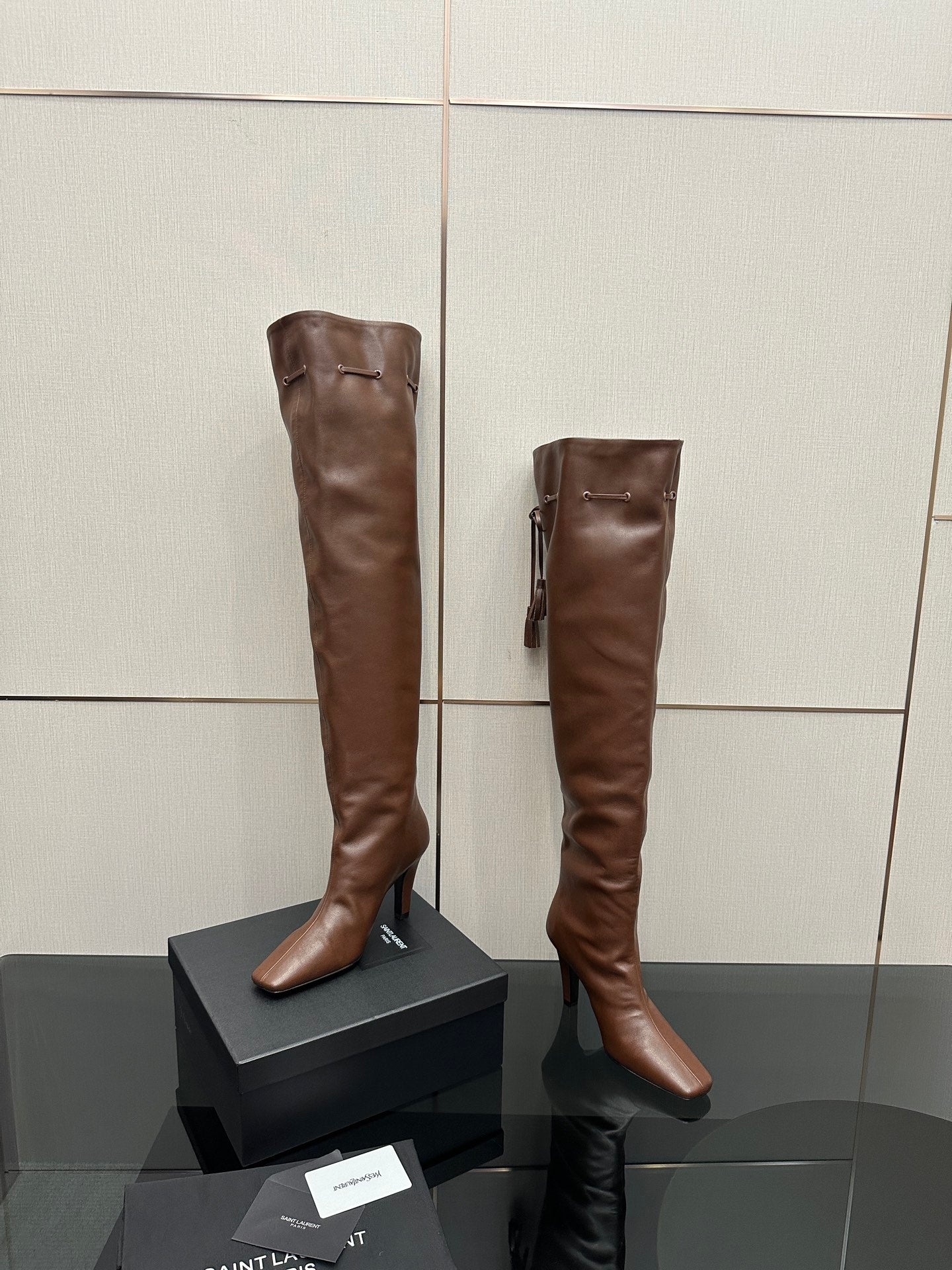 YSL knee-high leather boots, dark brown, front view pair on display boxes