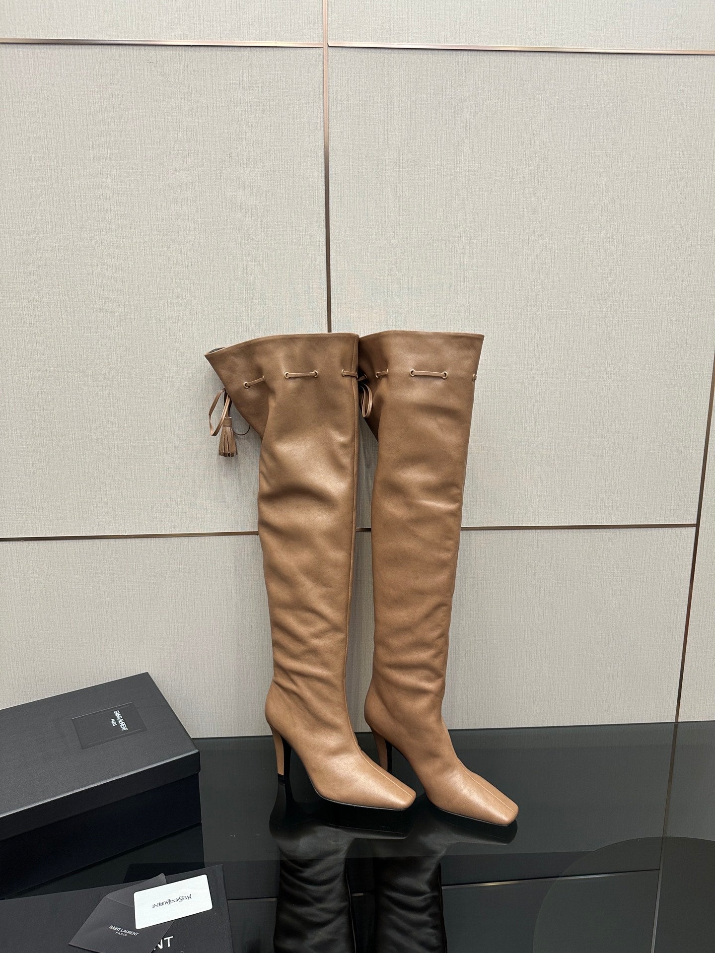 YSL taupe knee-high boots, stiletto heel, tassel tie detail, paired on display