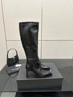 Knee-high black leather boot with slender heel and pointed toe on display.