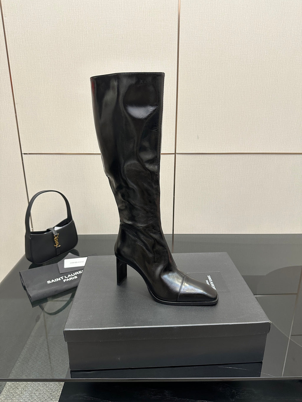 Single knee-high black leather boot with glossy finish and pointed toe on box.
