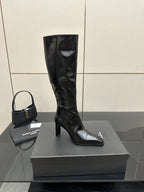Single knee-high black leather boot with glossy finish and pointed toe on box.