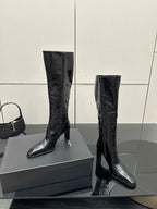 Knee-high black leather boots with slim heel and pointed toe, angled view.