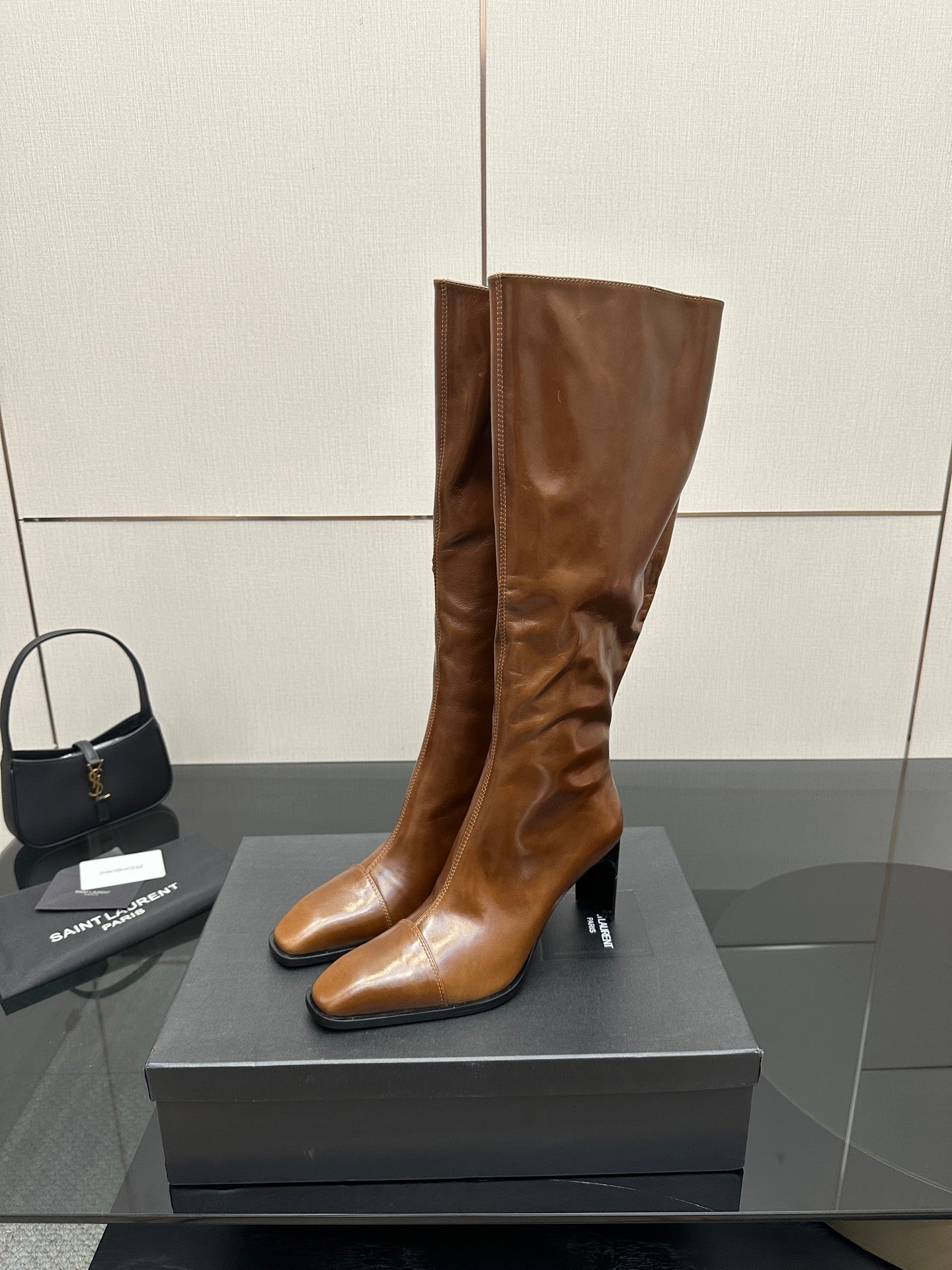 Brown knee-high leather boots with slim heel and pointed toe, standing on display box
