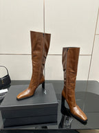 Brown knee-high leather boots with pointed toe and slim heel, standing on display box
