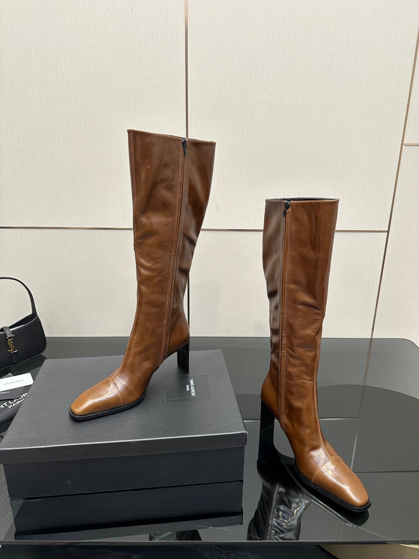 Brown knee-high leather boots with pointed toe and slim heel, standing on display box
