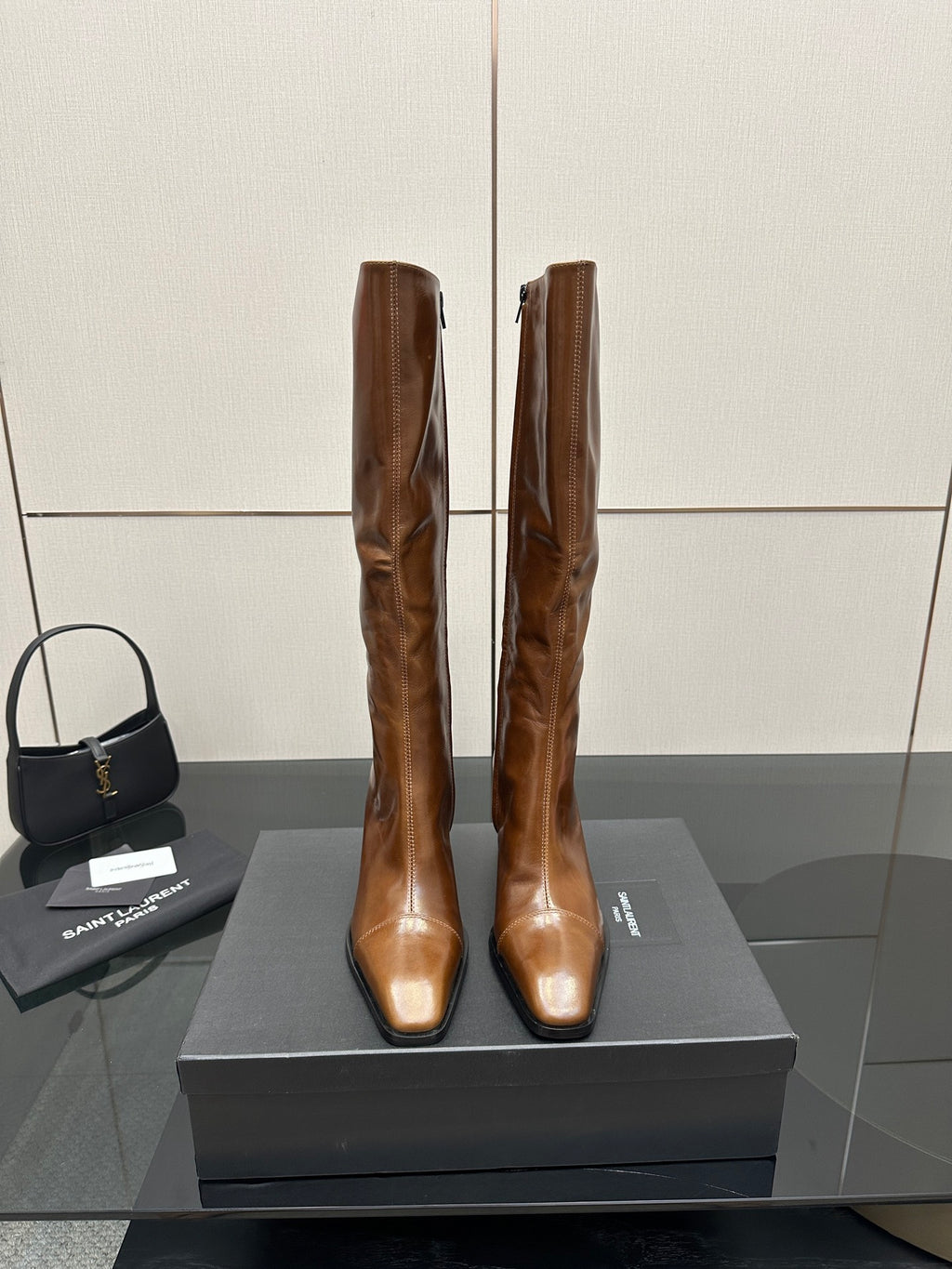 Brown knee-high leather boots with pointed toe and slim heel, side-by-side on box