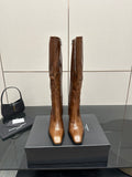 Brown knee-high leather boots with pointed toe and slim heel, side-by-side on box