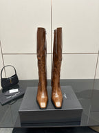 Brown knee-high leather boots with pointed toe and slim heel, side-by-side on box