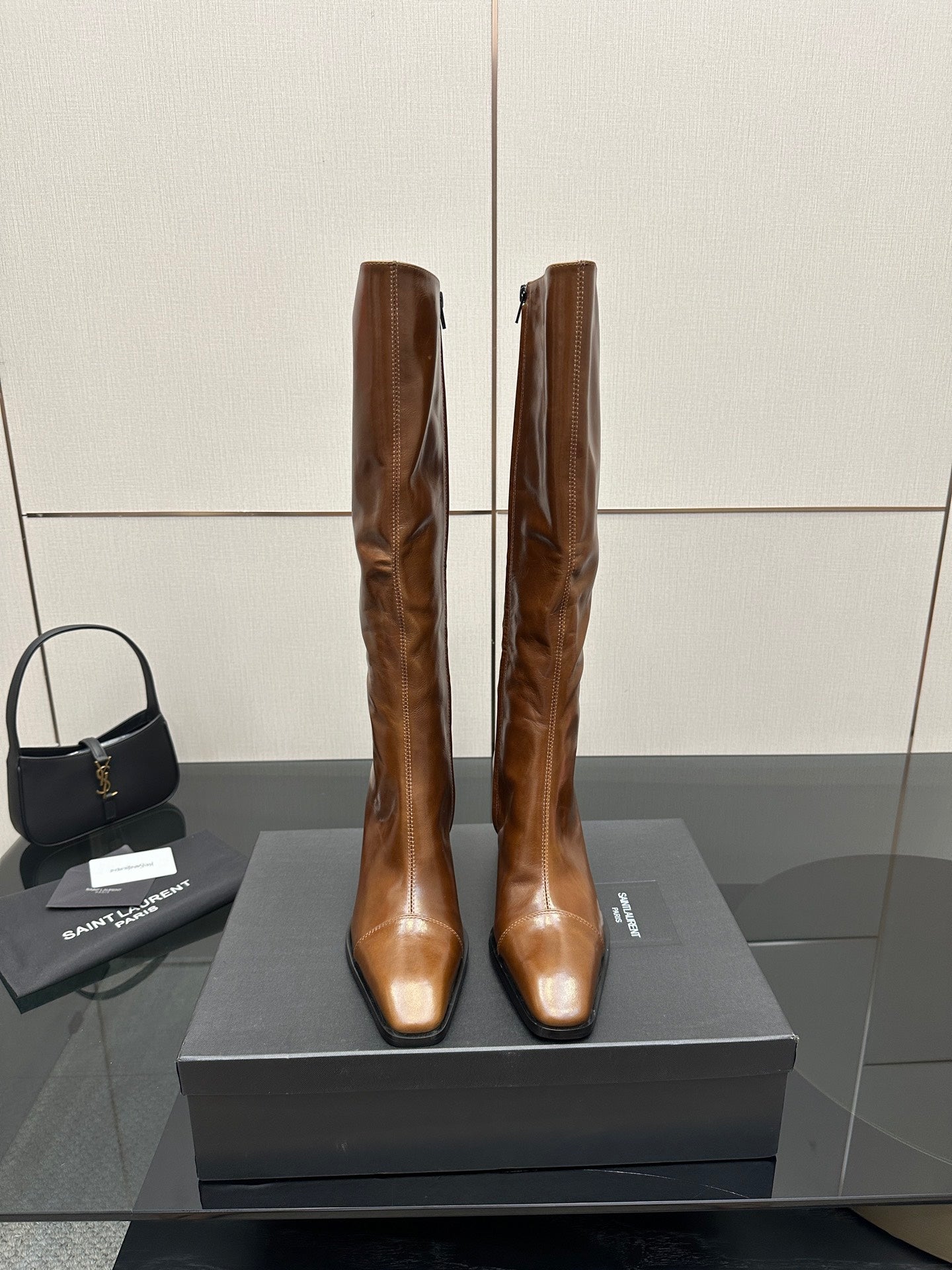 Brown knee-high leather boots with pointed toe and slim heel, side-by-side on box