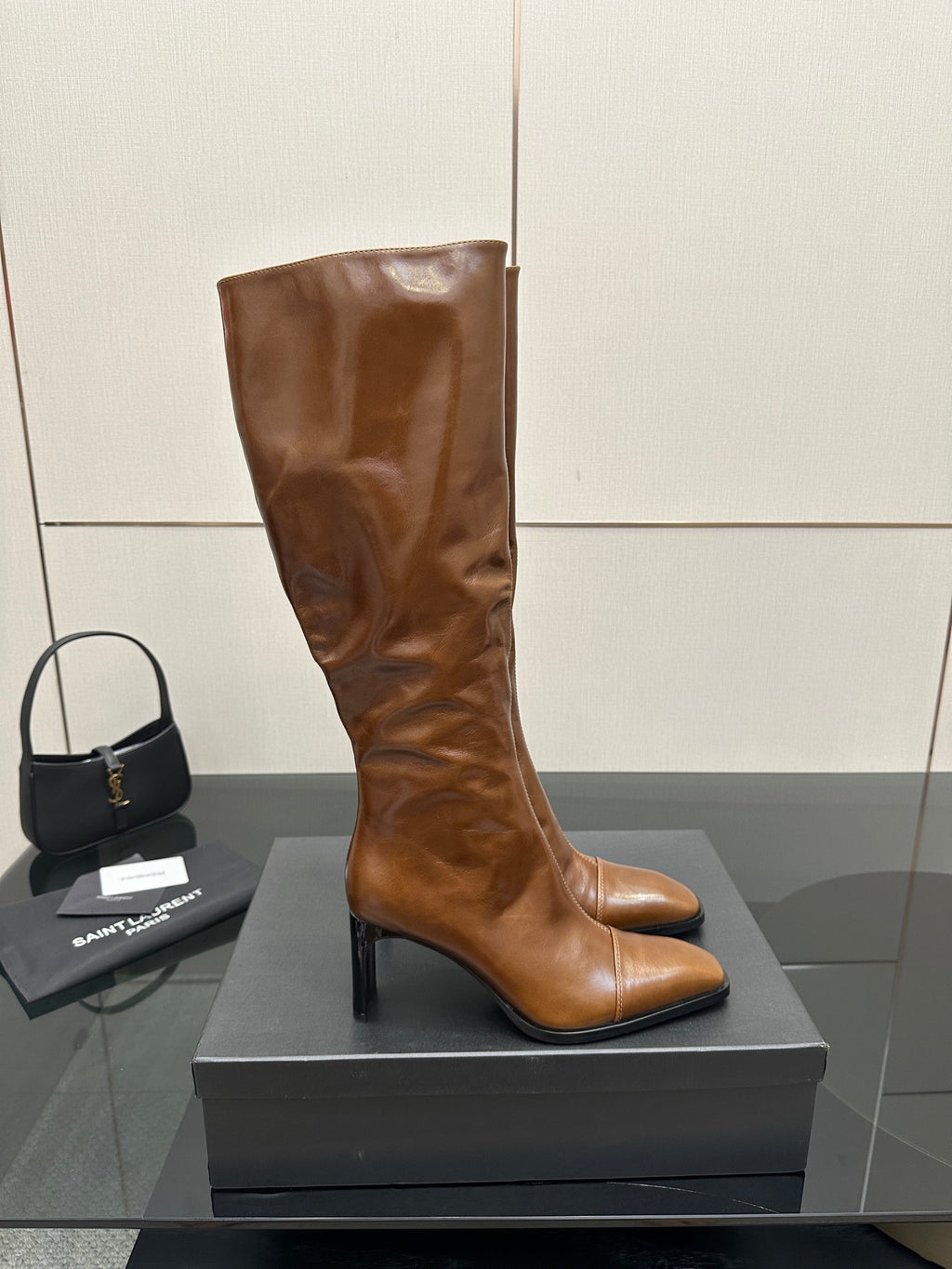 Brown knee-high leather boots with pointed toe and slim heel, front view on display box