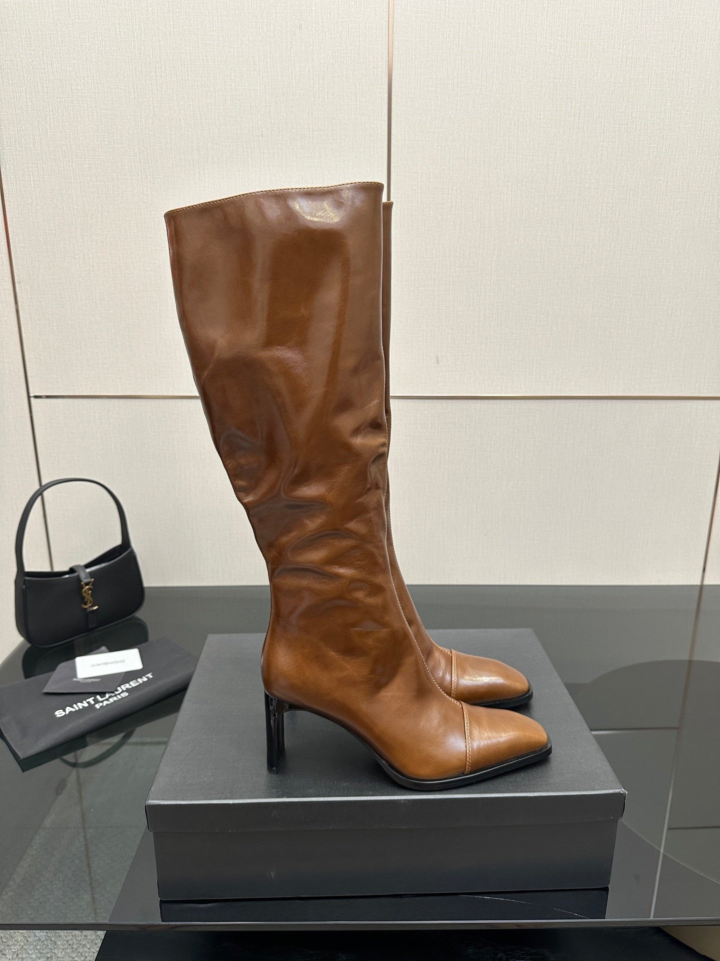 Brown knee-high leather boots with pointed toe and slim heel, front view on display box