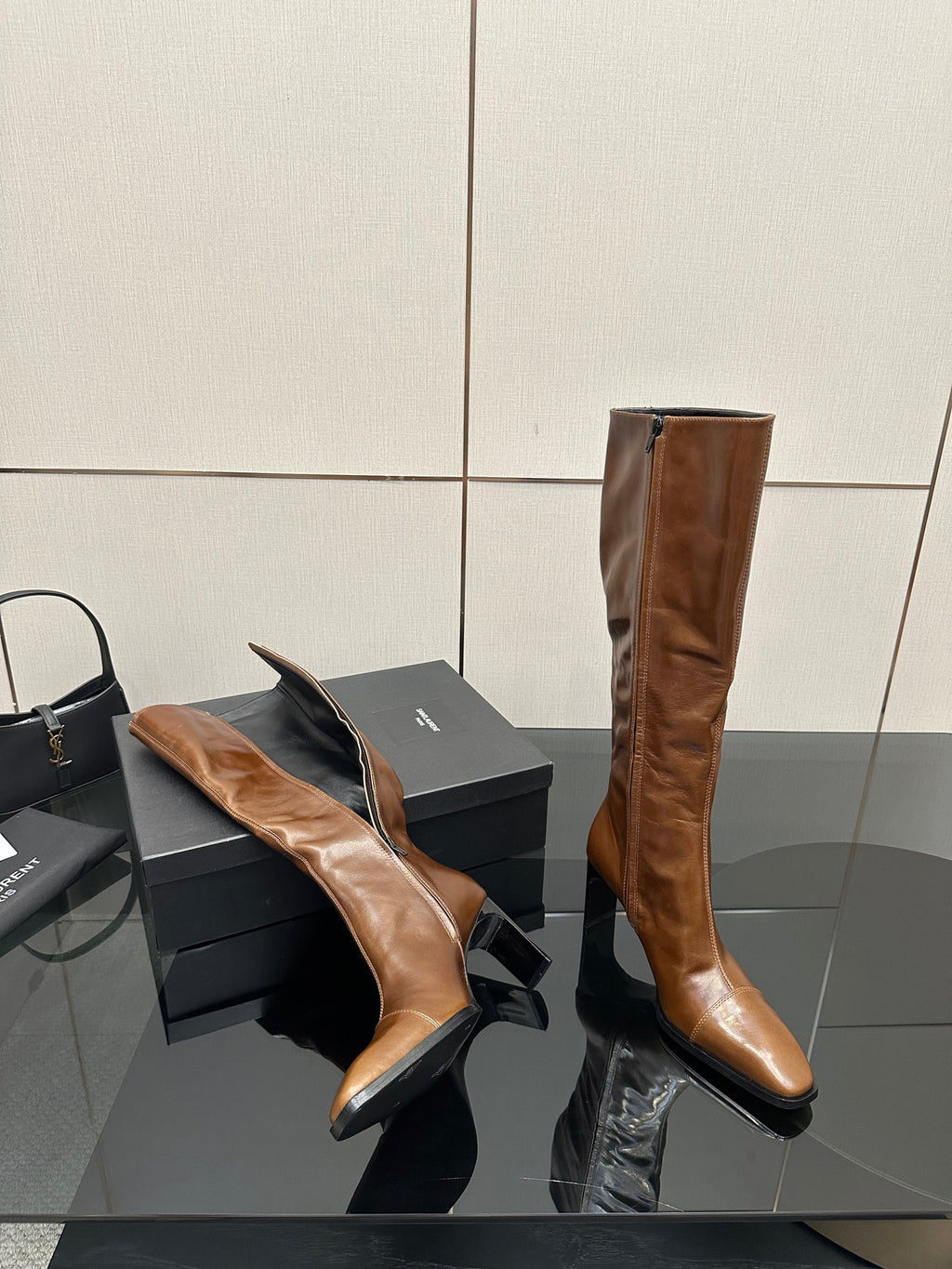 Brown knee-high leather boots with pointed toe and slim heel, one boot on its side