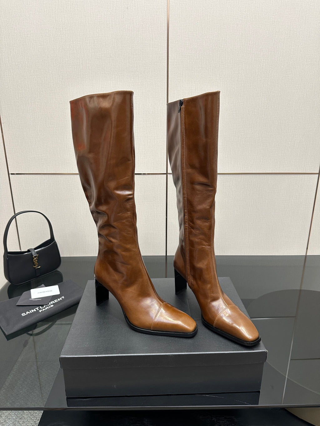 Brown knee-high leather boots with pointed toe and slim heel, angled side view on box