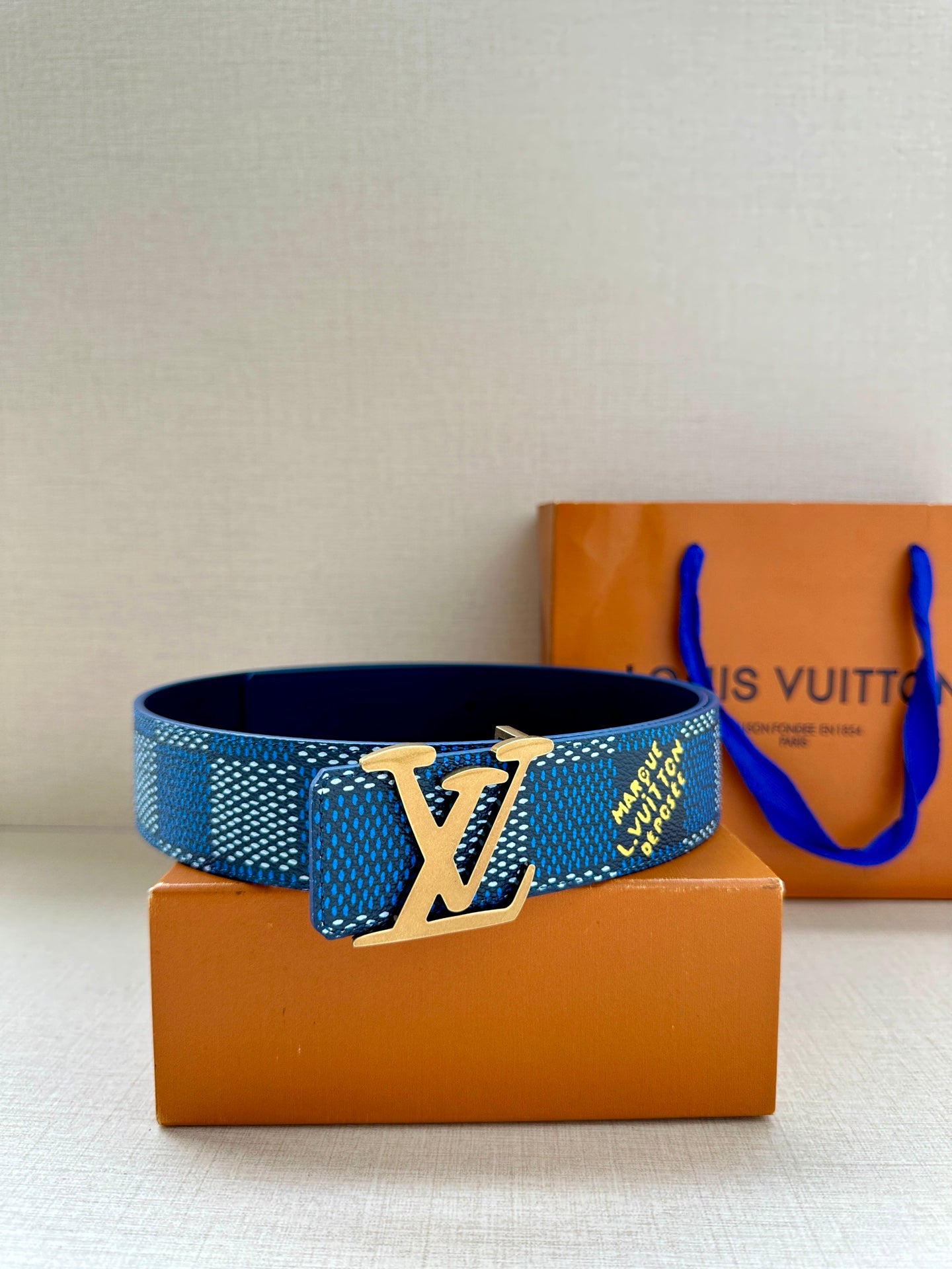 Blue Louis Vuitton belt with LV logo buckle displayed on box packaging.