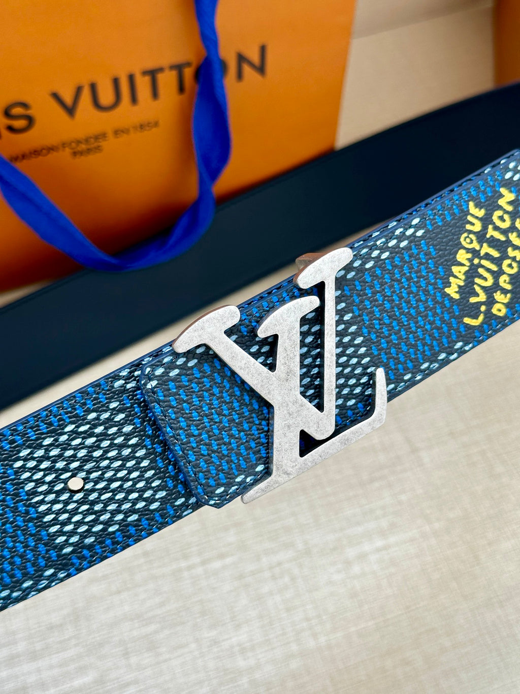 Blue woven Louis Vuitton belt with metal LV buckle on dark blue strap end.