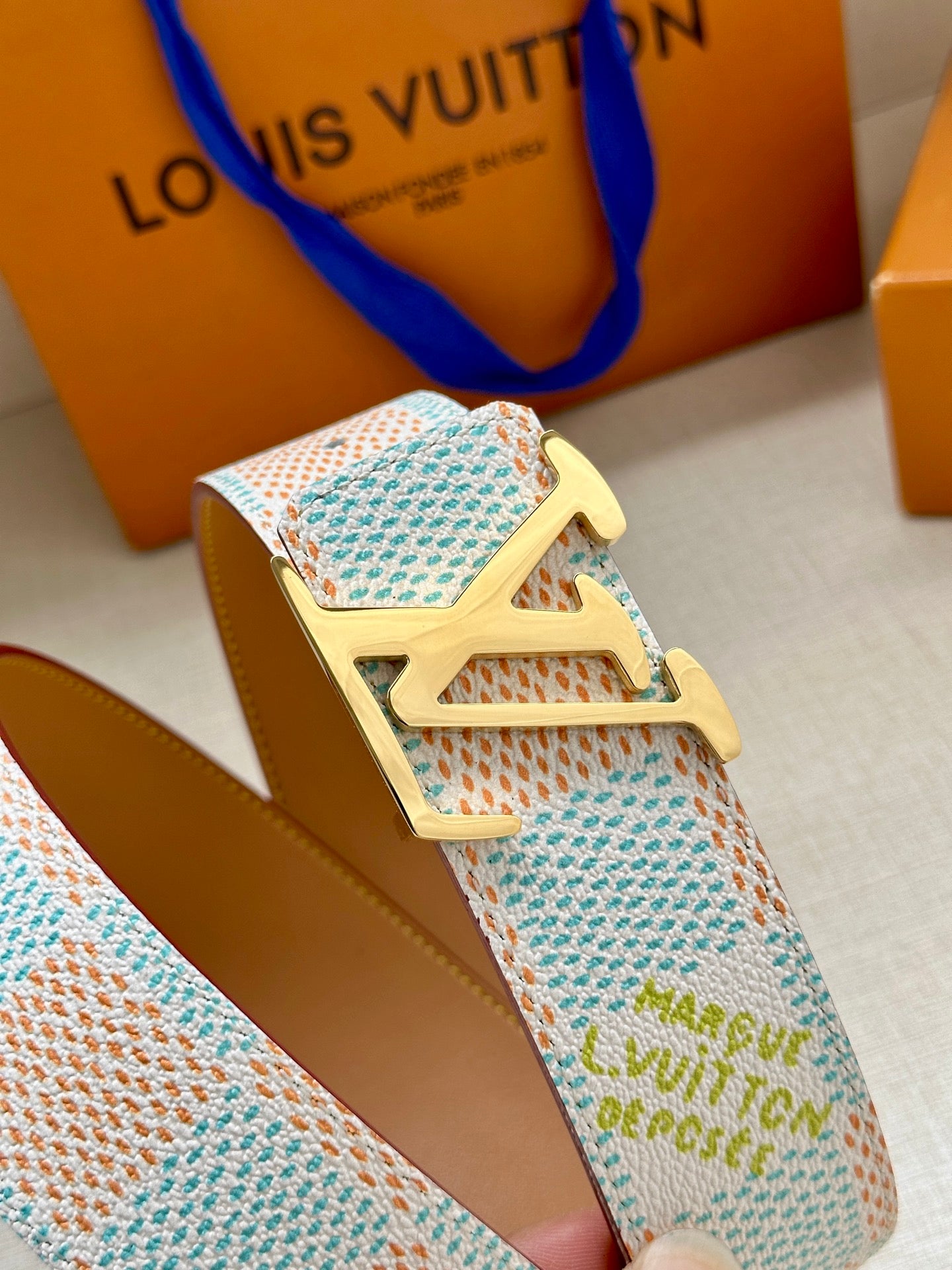 Louis Vuitton belt close-up: pastel blue patterned strap with gold LV buckle.