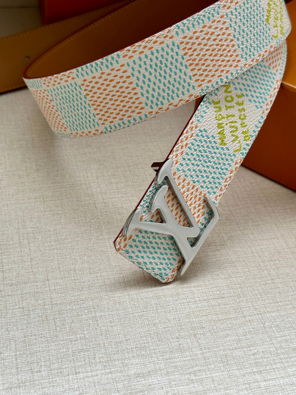 Louis Vuitton belt end close-up: pastel blue patterned strap with black LV buckle.