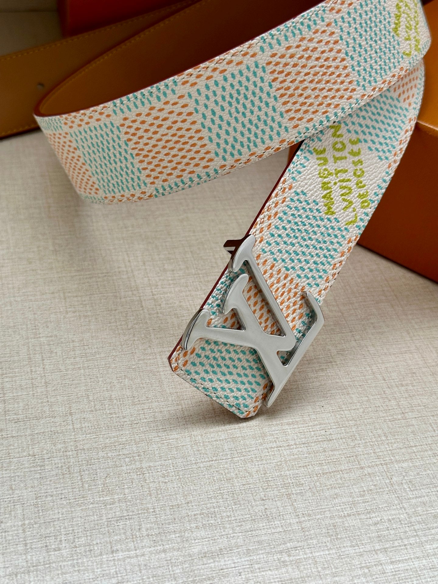 Louis Vuitton belt end close-up: pastel blue patterned strap with black LV buckle.