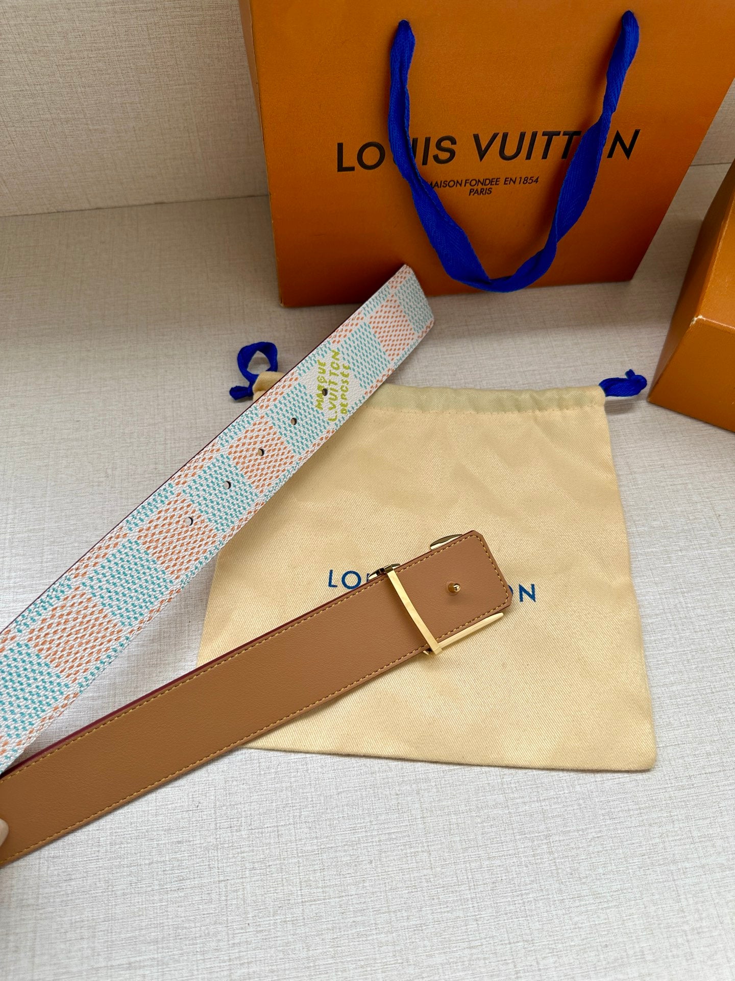 Louis Vuitton tan leather belt with gold buckle, shown with patterned strap.