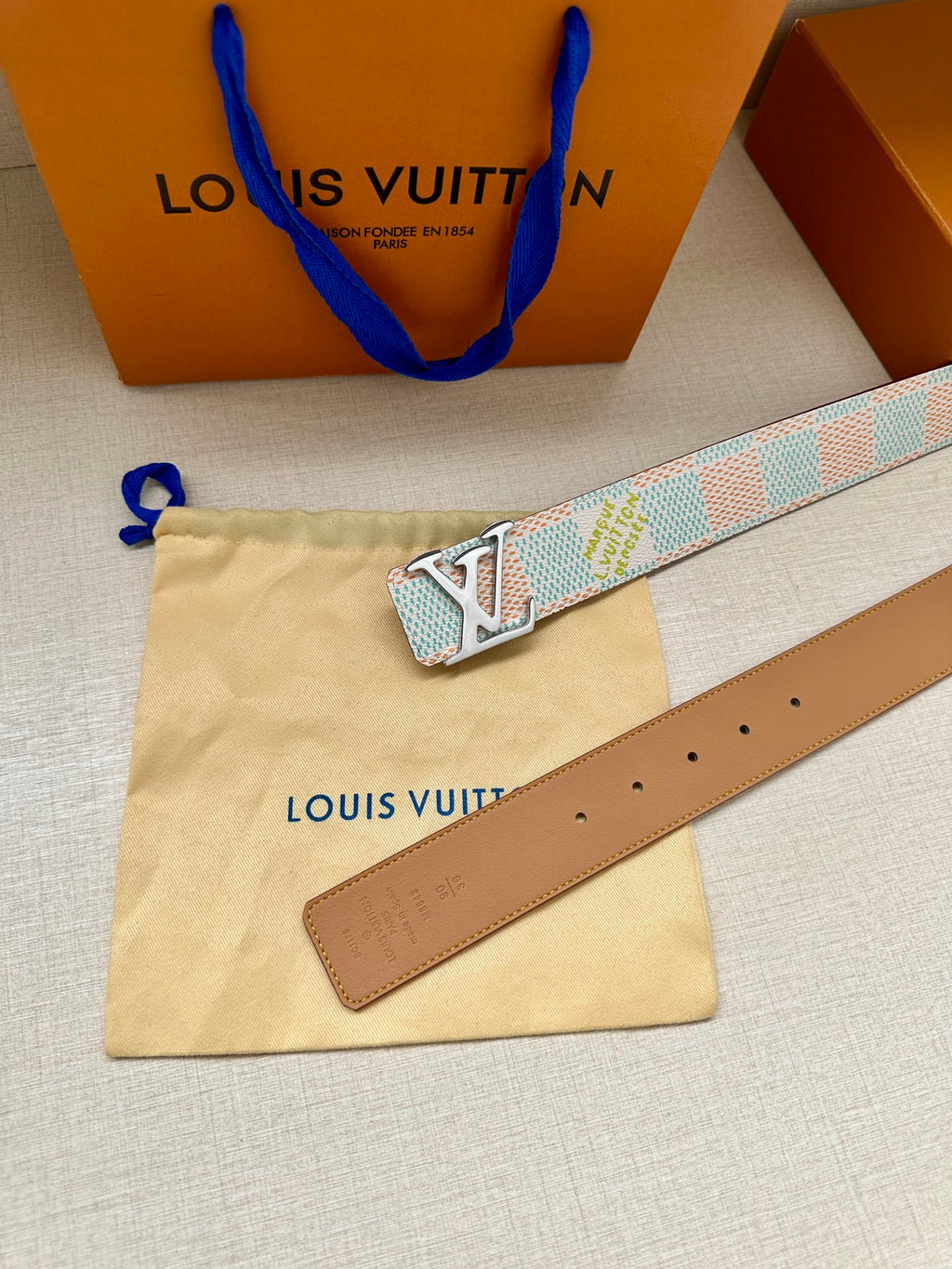 Louis Vuitton belt set on pouch: brown leather strap with holes and blue LV buckle.