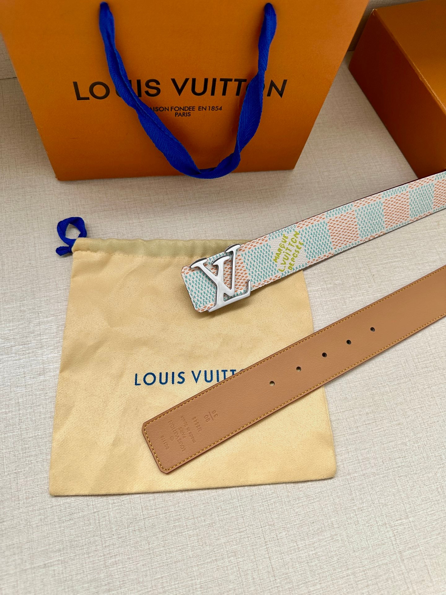 Louis Vuitton belt set on pouch: brown leather strap with holes and blue LV buckle.