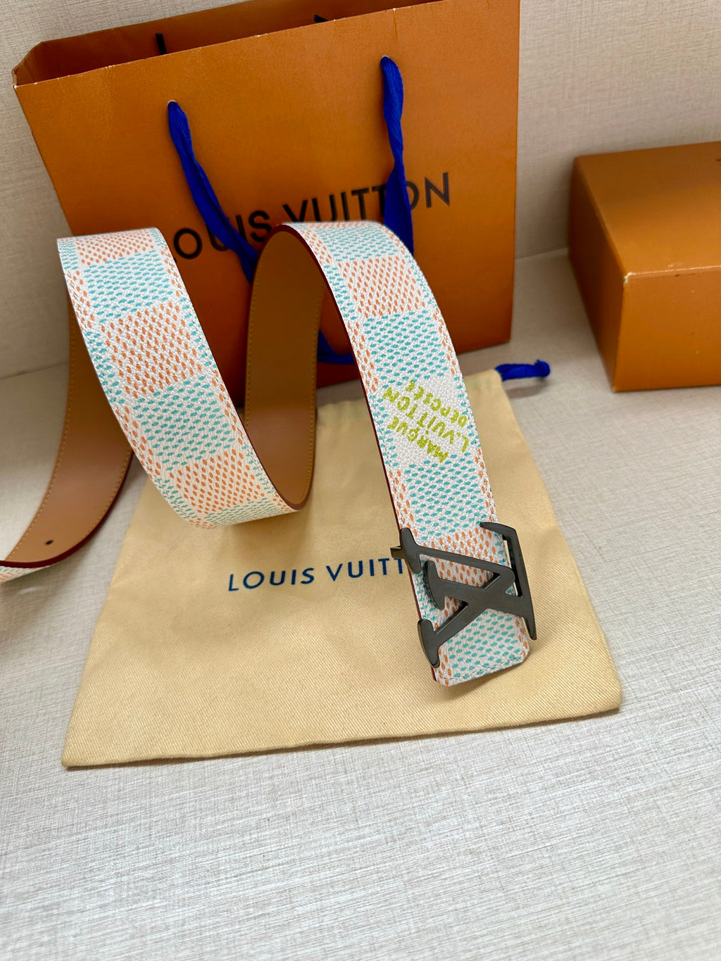 Louis Vuitton belt folded view: pastel blue patterned strap with black LV buckle.