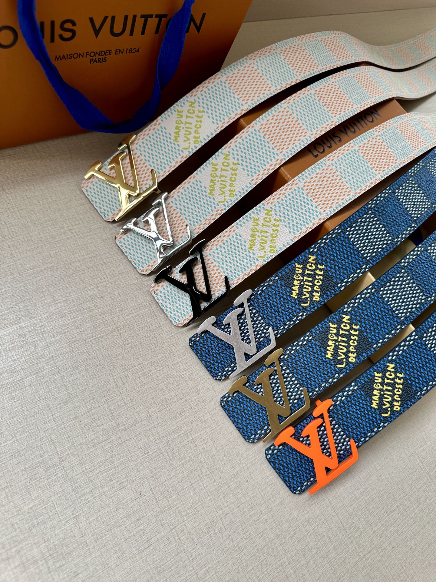 Two patterned canvas belts with gold-tone LV buckles, light blue and dark blue geometric straps