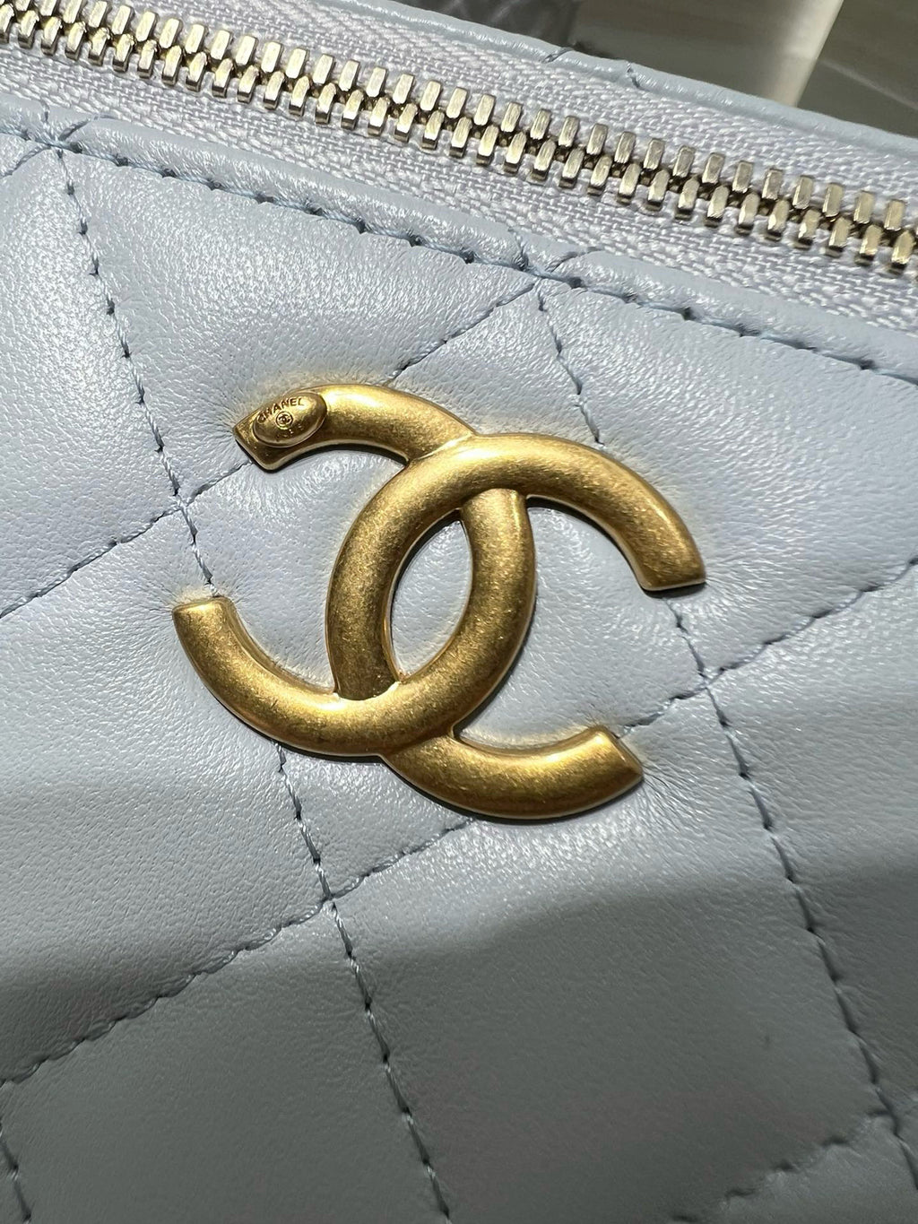 Gold CC logo on light blue quilted Chanel bag, textured leather close-up