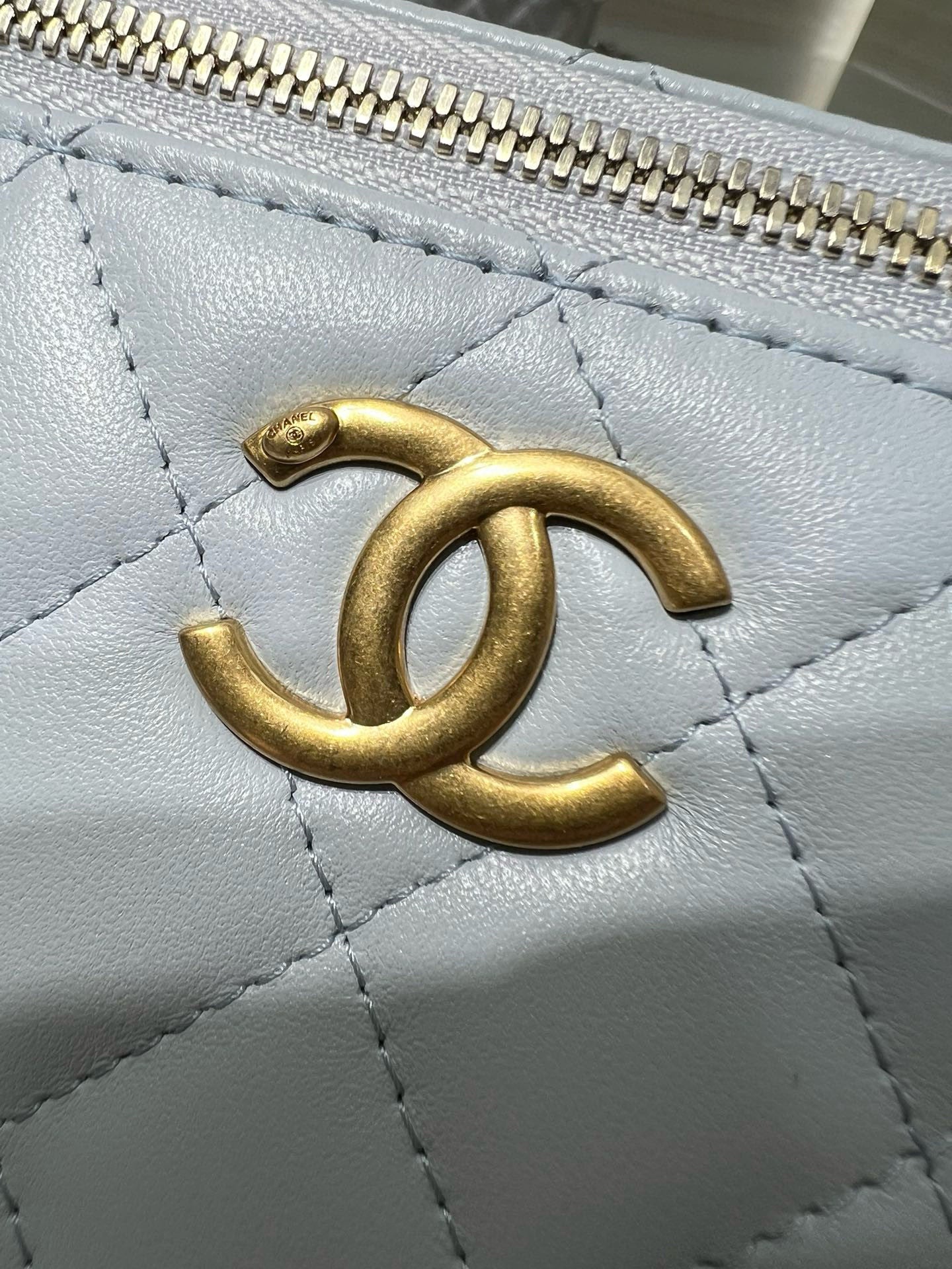 Gold CC logo on light blue quilted Chanel bag, textured leather close-up