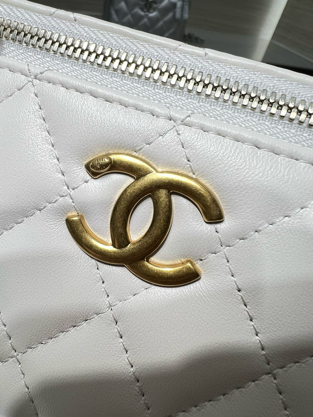 Close-up of white quilted bag with gold-tone CC-style clasp and metal zipper teeth