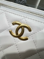 Close-up of white quilted bag with gold-tone CC-style clasp and metal zipper teeth
