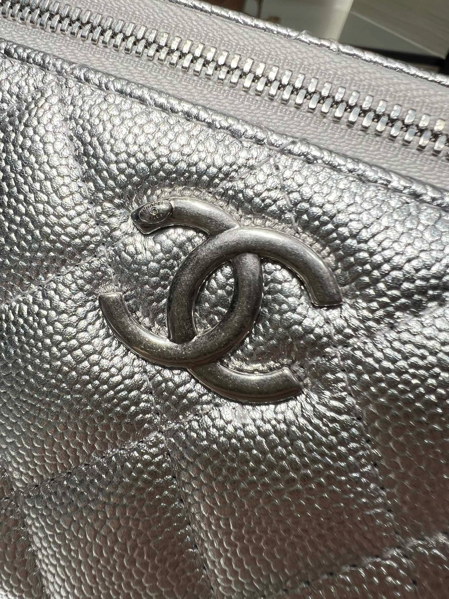 Chanel logo on quilted silver-tone leather flap with textured grain and zipper edge.