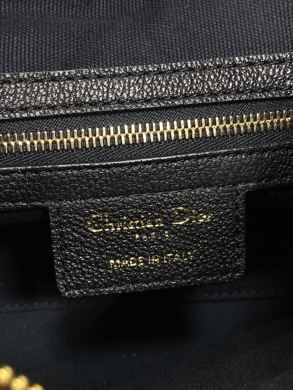 Black leather bag label with gold text and gold zipper trim detail