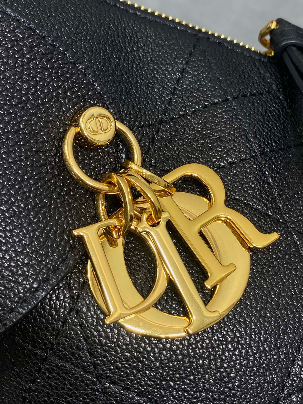 Close-up of gold-tone logo charm on black quilted leather bag