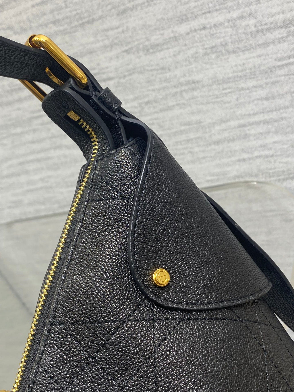 Black structured leather bag with curved top flap, gold zipper, and snap button