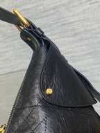 Black leather bag detail with gold D-ring, button, and textured stitching