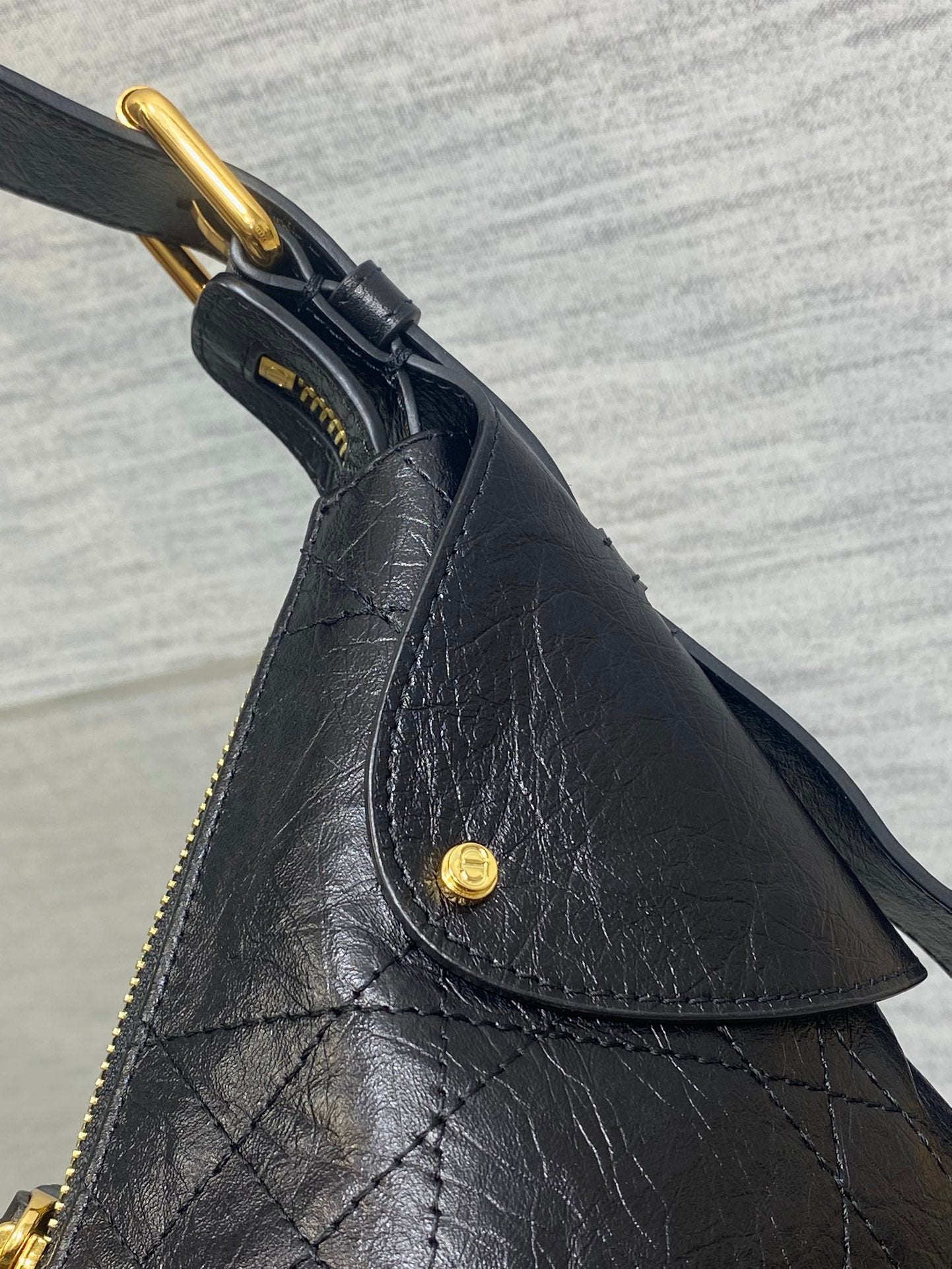 Black leather bag detail with gold D-ring, button, and textured stitching