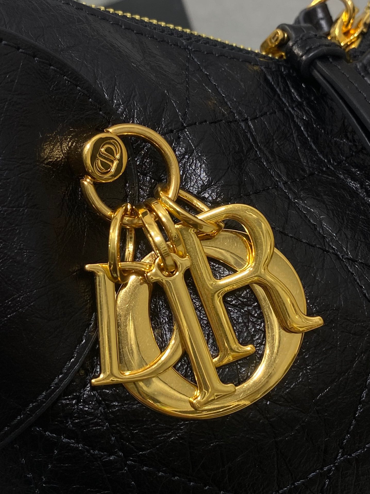 Black leather shoulder bag close-up with gold logo charm hardware
